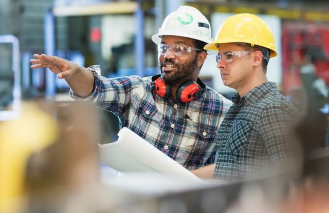 Arbeiter in Schutzausrüstung, die zusammen an einem technischen Projekt arbeiten