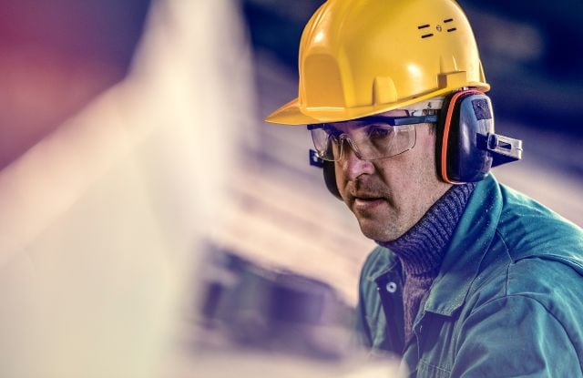 工业工人佩戴安全装备，如头盔、护耳和护眼等