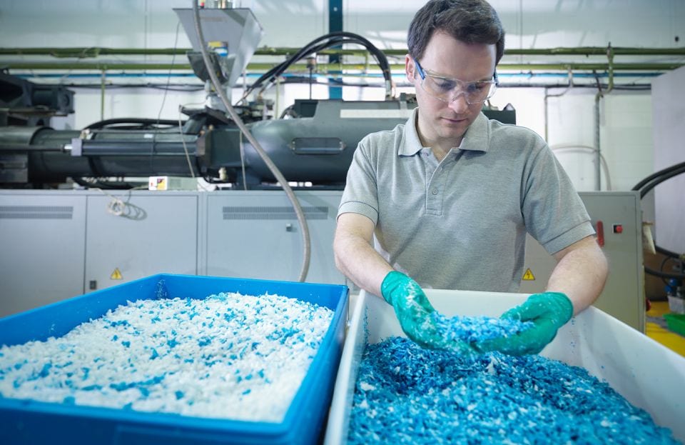 リサイクルプラスチックの粉砕再生材料の薄片を調べる従業員